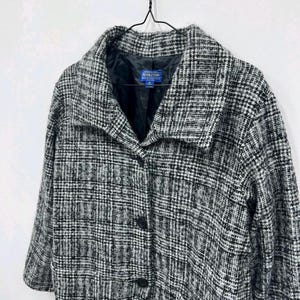 May include: A monochrome plaid coat with a wide collar and three black buttons. The coat is suspended on a black hanger. The brand name "Pendleton" is visible on the inside of the coat.