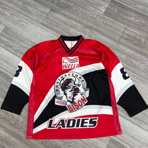May include: Red, black and white hockey jersey with the text "Basingstoke Bison" and "Wella" on the front. The jersey also has the number "8" on both sleeves and the word "LADIES" on the bottom.