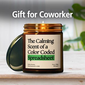 May include: A lit candle in a brown glass jar with a gold lid. The label reads "The Calming Scent of a Color Coded Spreadsheet." The text "Gift for Coworker" is at the top. The candle is 9 oz.