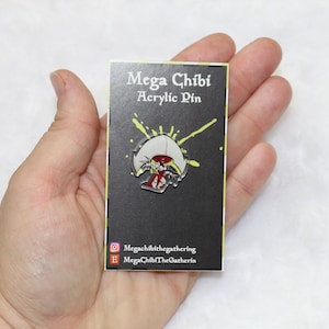 May include: A black card with white text that reads "Mega Chibi Acrylic Pin". A yellow and green splatter pattern is behind a white and red enamel pin of a mushroom with a face.