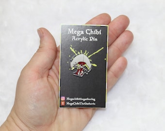 May include: A black card with white text that reads "Mega Chibi Acrylic Pin". A yellow and green splatter pattern is behind a white and red enamel pin of a mushroom with a face.