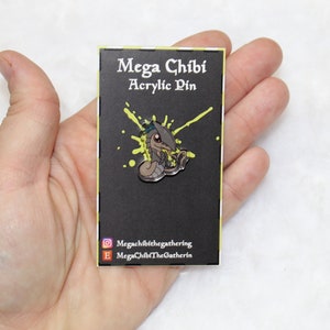 May include: Mega Chibi acrylic pin featuring a stylized serpent design with a blue and gray color scheme. The pin is on a black card with the text "Mega Chibi Acrylic Pin" and a yellow splatter design. The card also includes social media handles.