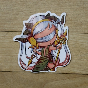May include: A blindfolded cartoon character with horns and long white hair holds a golden staff with a swirling design. The character is wearing a green and gold dress and has a pink and white background.