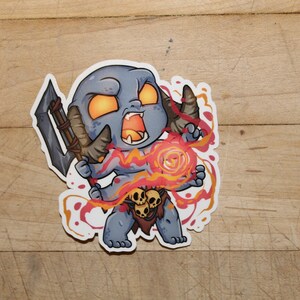 May include: A cartoon illustration of a blue demon with horns, holding a weapon and a glowing orb. The demon is surrounded by red and orange flames.