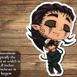 May include: A sticker of a green-skinned, black-haired woman with closed eyes, wearing a black and green outfit. She is holding a small, black and gold creature in her arms. The sticker is approximately 2.8 inches in size.