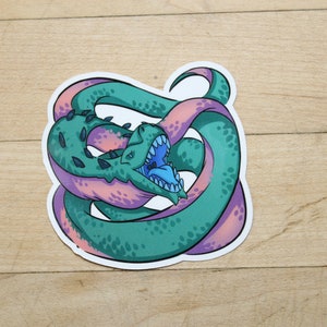 May include: A sticker featuring a green and pink cartoon creature with a large mouth and sharp teeth. The creature is curled up in a circle, with its tail in its mouth.
