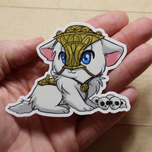 Op de afbeelding: Een witte kat met een gouden helm, een blauw oog en een gouden ketting. De kat zit op een witte achtergrond met een stapel zwarte schedels voor hem.