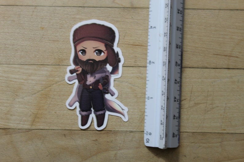 May include: A cartoon sticker of a person wearing a brown hat and a brown beard, holding a small axe. The person is wearing a brown and white jacket and brown pants. The sticker is on a wooden surface.