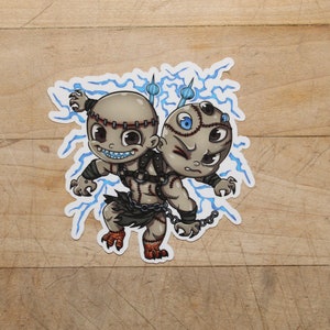 May include: A cartoon sticker of two stitched-together monsters with blue lightning bolts around them. The monster on the left has a stitched-up face with a toothy grin and is holding a chain. The monster on the right has one eye and a stitched-up face with a frown.