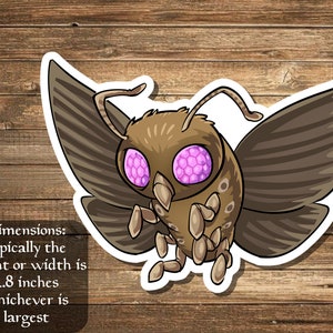 May include: A brown and gray moth sticker with large pink eyes. The moth has a fuzzy body and wings with a striped pattern. The sticker is approximately 2.8 inches in size.