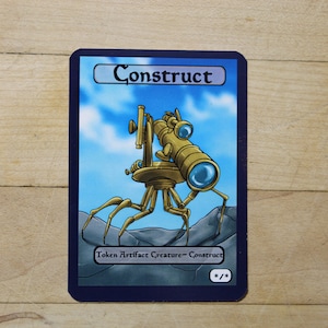 Puede incluir: Una carta azul y blanca de Magic: The Gathering con el texto "Construct" y un dibujo de un robot dorado con un telescopio en la espalda. El texto de la carta dice "Ficha Criatura Artefacto - Construct".