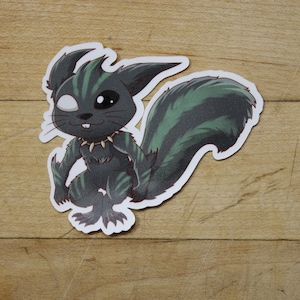 May include: A black and green cartoon sticker of a creature with a spiky tail and a white eye. The creature has a spiked collar and is sitting on its haunches.
