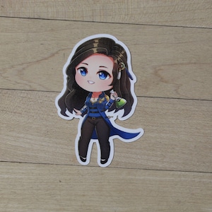 May include: A sticker featuring a cartoon illustration of a woman with long brown hair, wearing a blue and gold jacket, black pants, and holding a green potion bottle.