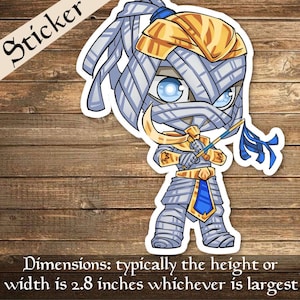 Op de afbeelding: Een cartoon sticker van een mummie met blauwe ogen, die een gouden kroon draagt en een blauwe staf vasthoudt. De mummie draagt witte banden en een blauwe sjerp om de taille. De sticker is ongeveer 2,8 inch breed.