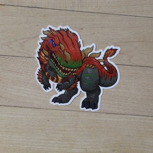 May include: A red and black cartoon dinosaur sticker with green and yellow accents. The dinosaur has a fierce expression and is shown with its mouth open.