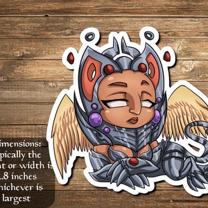 May include: A sticker of a cartoon cat with wings, wearing silver armor and a red gem on its chest. The cat has brown skin, closed eyes, and a pink nose. The sticker is 2.8 inches in size.
