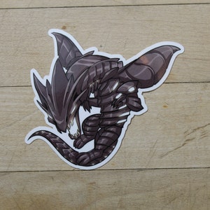 May include: A black and gray cartoon dragon sticker with a fierce expression. The dragon has sharp teeth and claws, and its wings are spread out.