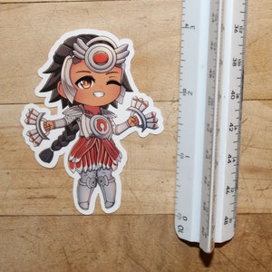 Pode incluir: Um adesivo com um personagem de desenho animado com cabelo castanho, vestindo uma roupa branca e vermelha com um grande c&iacute;rculo vermelho no peito. Ela est&aacute; segurando um leque branco e vermelho em cada m&atilde;o e tem uma express&atilde;o piscando.