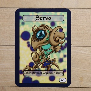 May include: A gold and green robot creature with a large blue eye. The card reads "Servo" and "Token Artifact Creature - Servo 1/1".