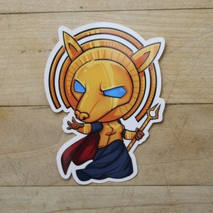 May include: A cartoon sticker of a golden, anthropomorphic creature with a lion head, blue eyes, and a red cape. The creature is holding a golden trident and is standing on a blue and gold patterned background.
