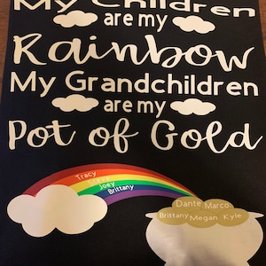Pode incluir: Tecido preto com texto branco que diz "Meus filhos são meu arco-íris. Meus netos são meu pote de ouro." Um arco-íris com nomes escritos nele leva a um pote de ouro com moedas de ouro que têm nomes escritos nelas.