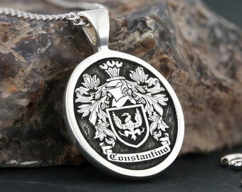 May include: Silver pendant necklace with a black and white coat of arms featuring a bird and the name "Constantino" inscribed on a banner.