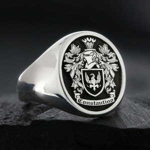 May include: A silver signet ring with a black oval top featuring a coat of arms with a bird and the text "Constantino".