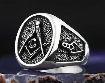 Può includere: Un anello massonico d'argento con finitura testurizzata. L'anello presenta un design a squadra e compasso con una lettera 'G' al centro. L'anello ha anche un piccolo design a cazzuola sul lato.