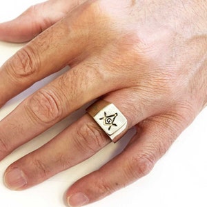 May include: A silver ring with a square-shaped top featuring a gold Masonic symbol.