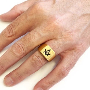 May include: A gold ring with a square-shaped band featuring a black Masonic symbol.