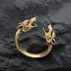 Könnte beinhalten: Ein goldfarbener Ring mit zwei sich gegenüberstehenden Wolfsköpfen. Der Ring ist offen und verstellbar.