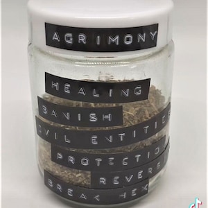 以下が含まれることがあります： 白い蓋のついたガラス瓶に乾燥ハーブが入っています。瓶には、「AGRIMONY」、「HEALING」、「BANISH」、「EVIL ENTITIES」、「PROTECTION」、「REVERSE」、「BREAK HEX」という黒いラベルが貼られています。