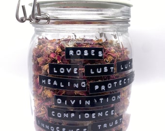 May include: A glass jar filled with dried rose petals. The jar has labels with the words "Roses", "Love", "Lust", "Healing", "Protection", "Divination", "Confidence", "Innocence", "Trust", "Psychic", and "Power".