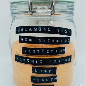 May include: A clear glass jar with a metal clasp, filled with a light brown powder. Black labels on the jar list various intentions: Galangal Root, Hex Breaking, Protection, Psychic Powers, Lust, Health, Power, and Money.