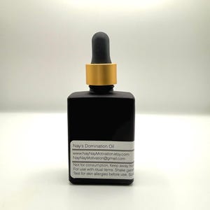 Può includere: Un flacone quadrato in vetro nero opaco con un collare color oro e un contagocce nero. Un'etichetta rettangolare bianca sulla parte anteriore riporta il testo Nay's Domination Oil, dettagli del sito web e dell'email, e istruzioni di sicurezza.