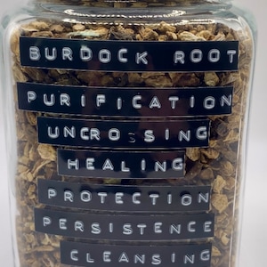 以下が含まれることがあります： 乾燥したゴボウの根が詰まったガラス瓶。瓶には銀色の蓋と、「ゴボウの根」、「浄化」、「解呪」、「治癒」、「保護」、「忍耐」、「浄化」と書かれたラベルが付いています。