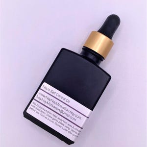 Op de afbeelding: Een zwarte vierkante glazen fles met een goudkleurige kraag en zwarte druppelaar. Het etiket luidt "Nay's Self Control Oil" en bevat een website en e-mailadres. De fles is voor ritueel gebruik.