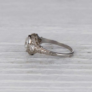 May include: A vintage-style engagement ring with a large, oval-shaped center stone and two smaller accent stones. The ring is made of silver and has intricate details.
