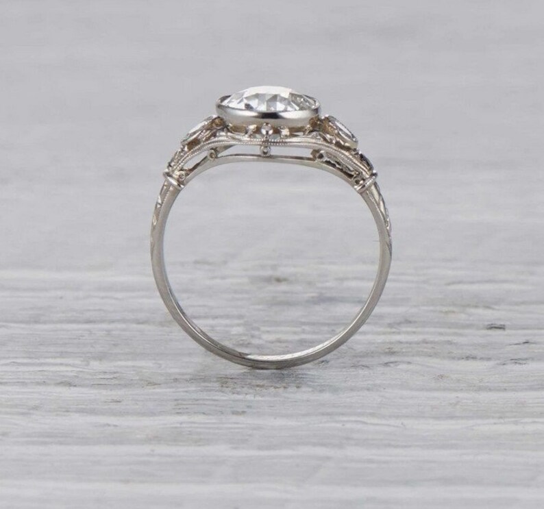 May include: A silver engagement ring with a large, round, clear center stone and smaller stones on the band. The ring has a delicate, intricate design.