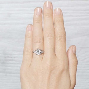 May include: A silver engagement ring with a large round center stone and smaller stones set in a halo around it.