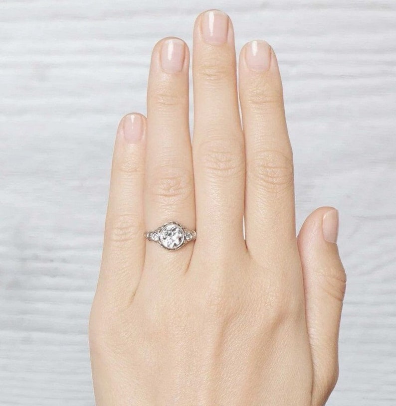 May include: A silver engagement ring with a large round center stone and smaller stones set in a halo around it.