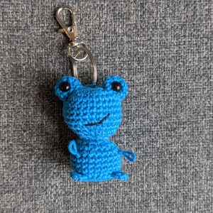 May include: A blue crocheted frog keychain with black eyes and a silver key ring.