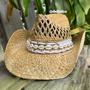 May include: A straw cowboy hat with a white band and gold accents. The band is decorated with small white seashells and gold beads.