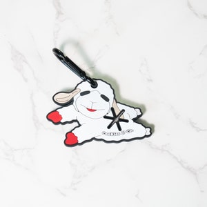 May include: White plush sheep keychain with red feet and a black clip. The sheep is smiling and has a black star on its chest. The text "Cookies & Co." is printed on the sheep's belly.