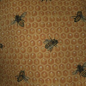 May include: A fabric pattern featuring a repeating honeycomb design in shades of golden yellow and brown. The background consists of a hexagonal grid, with multiple detailed illustrations of honeybees scattered across the surface in various orientations.