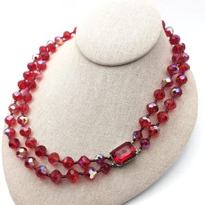 May include: A double strand necklace made of red faceted glass beads with a large red faceted glass pendant in the center.