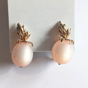 May include: A pair of gold tone earrings with a pink pearlescent sphere and a pineapple design.