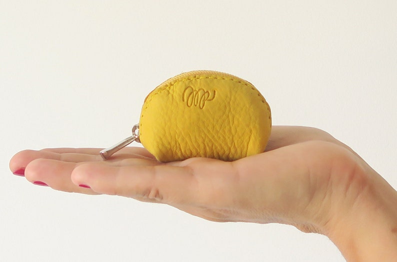 May include: A small, yellow leather coin purse with a zipper closure. The purse has a small, embossed logo on the front.