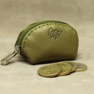 May include: A small, olive green leather coin purse with a zipper closure. The purse has a stitched seam around the edge and the word "Cozy" embossed on the front.