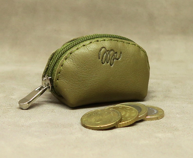 May include: A small, olive green leather coin purse with a zipper closure. The purse has a stitched seam around the edge and the word "Cozy" embossed on the front.